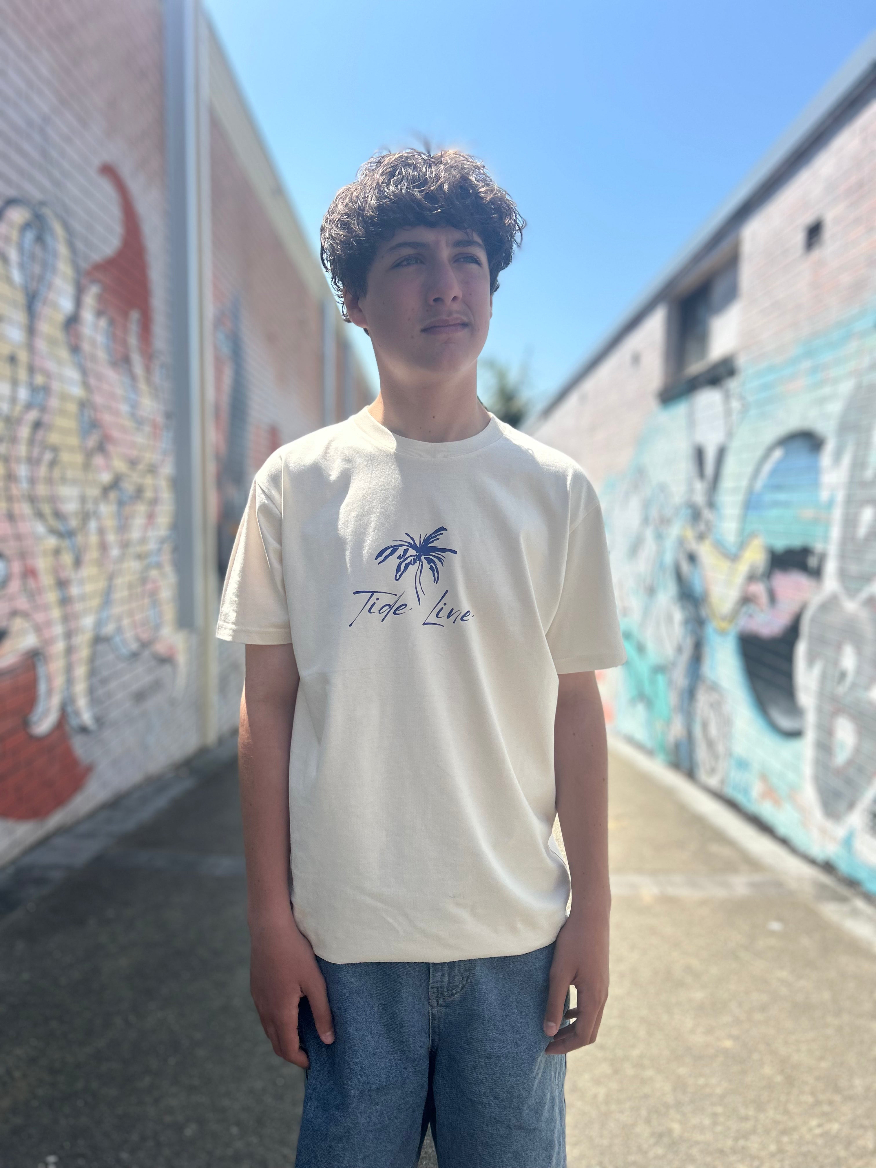 Person wearing a natural colour t-shirt with a graphic design in front of a colourful mural.