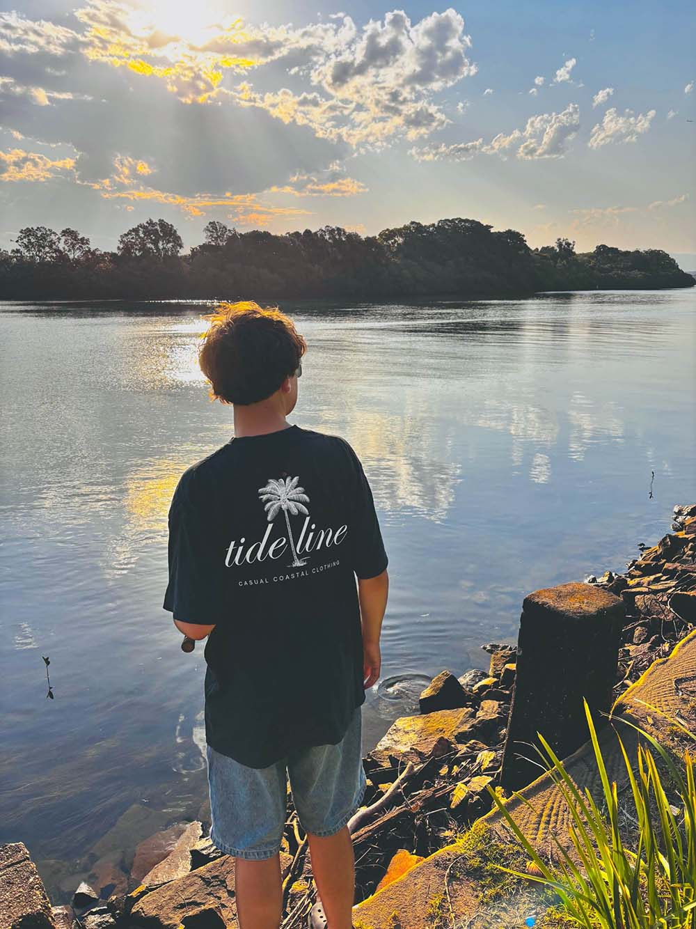 Male model wearing a relaxed fit Paradise Beach Unisex Coastal Graphic T-Shirt on the river fishing
